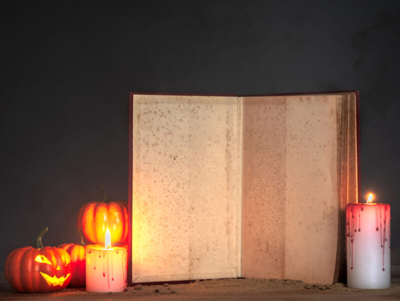 An old open book surrounded by candles and Halloween pumpkins
