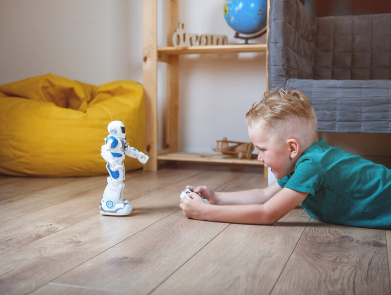 A young boy lying on the floor and playing with a remote-controlled robot