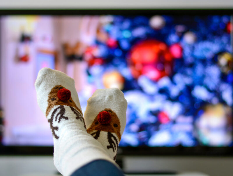 Someone with their feet up in front of the TV with Christmas socks on