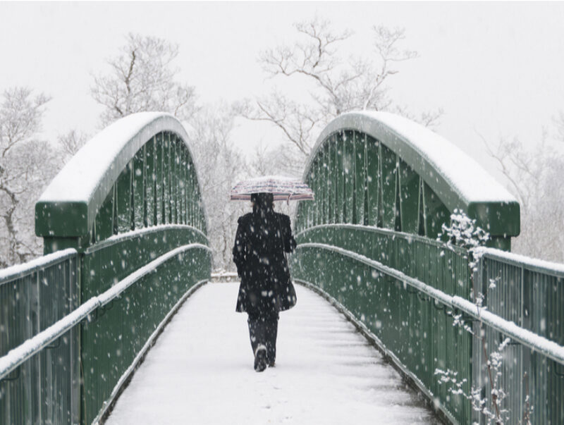 A woman walking across a bridge in heavy snow