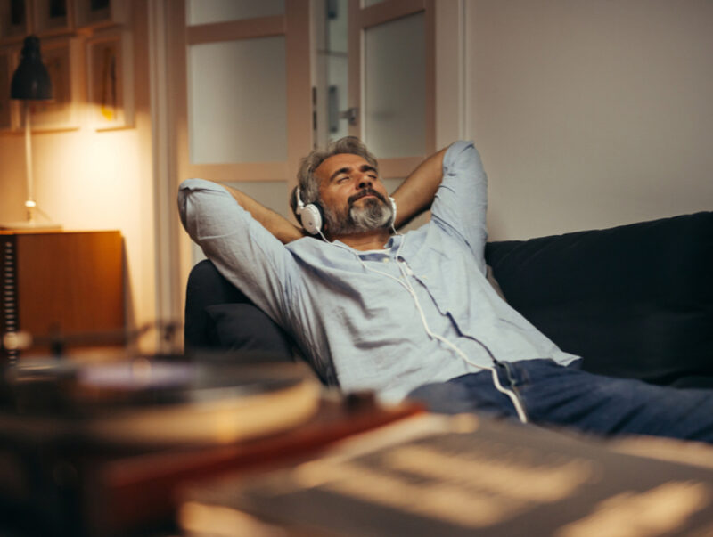 A man lies on the sofa listening to headphones