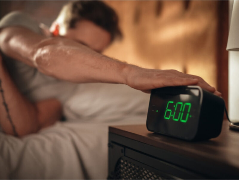 A man in bed reaches over to turn off his alarm clock