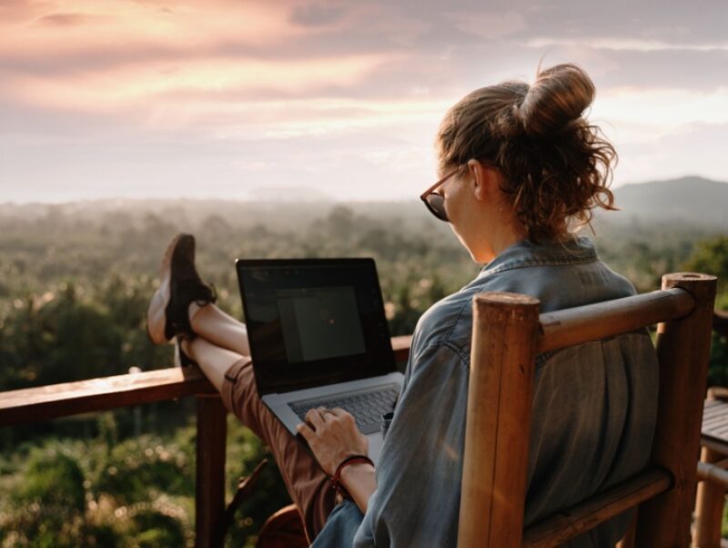 A woman with her feet up on a balcony working on a laptop